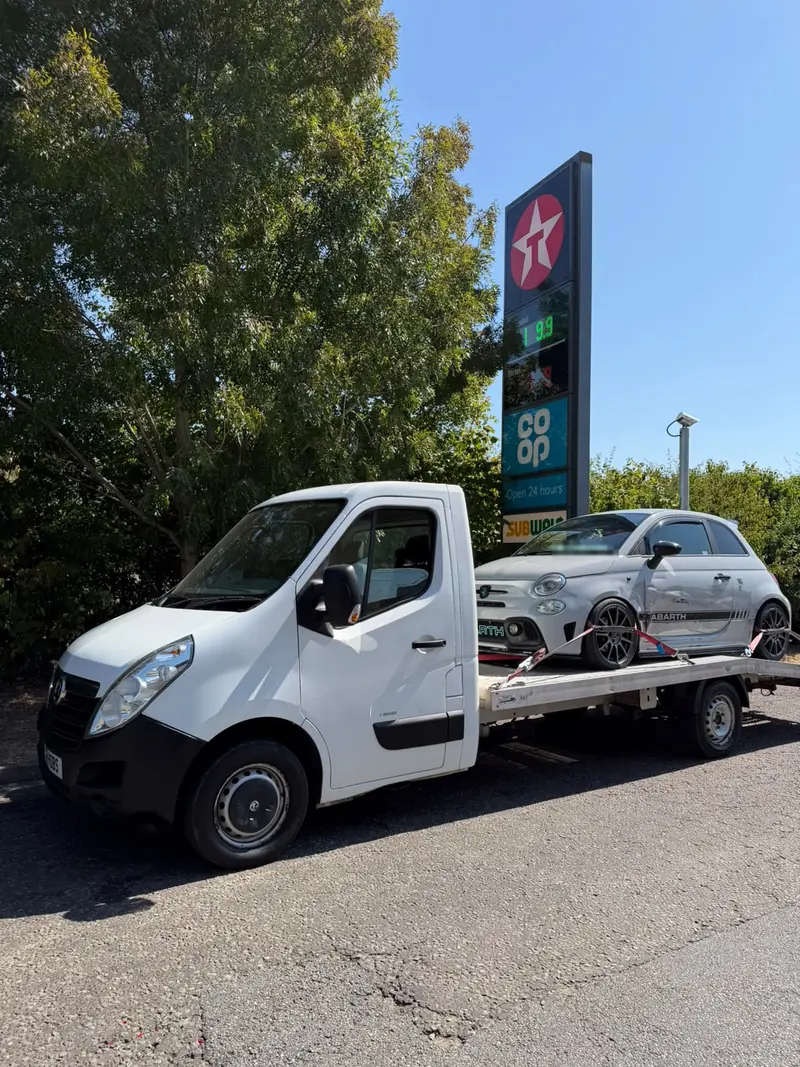 Grey Abarth 595 with a damaged door loaded on the recovery truck at a petrol station