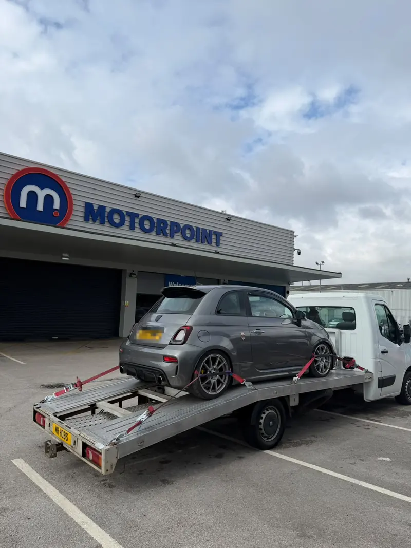 Grey Abarth 595 loaded on the recovery truck outside a car dealership