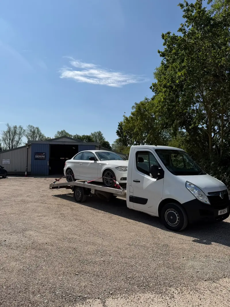 White BMW 1 Series on the recovery truck outside a motorsport garage