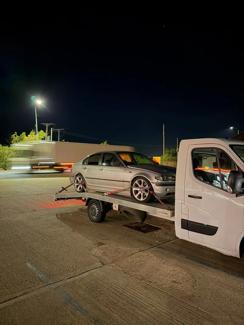 Silver BMW 3 Series secured on the recovery truck at night as a lorry passes