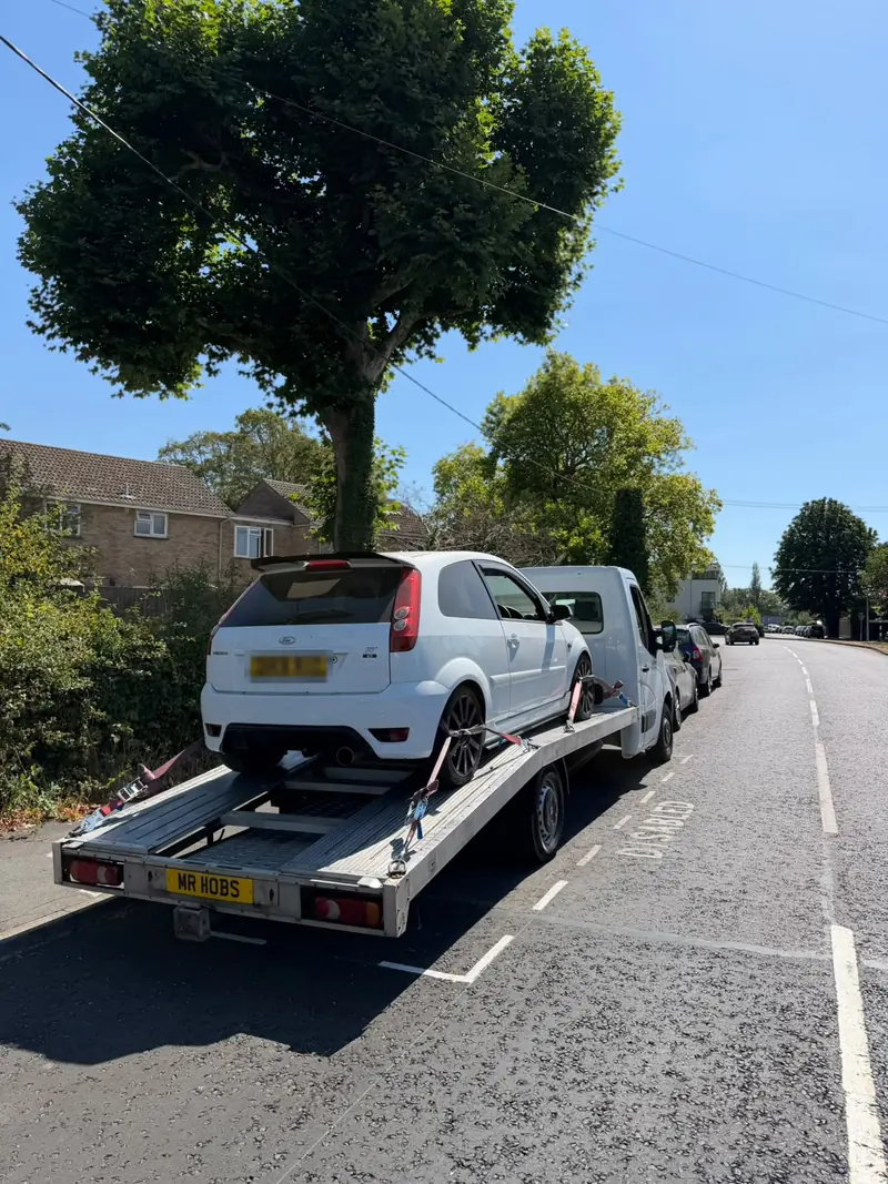 White Ford Fiesta ST strapped to the recovery truck on a residential street