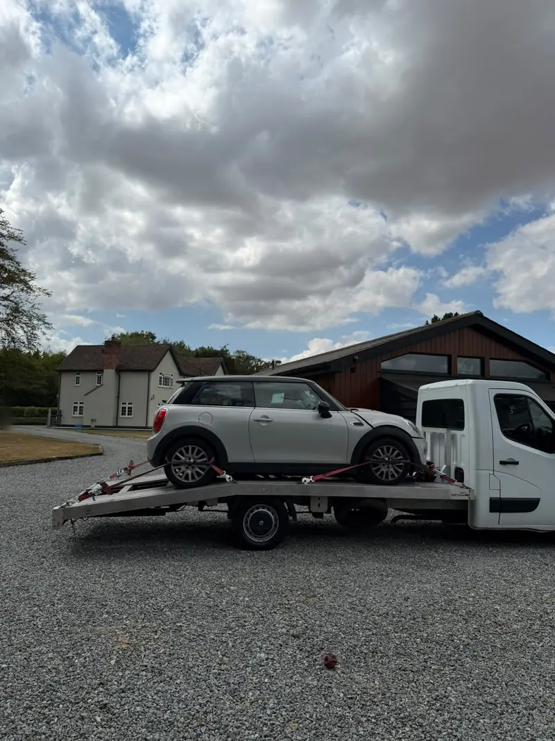 Silver Mini with front-end damage loaded on the recovery truck on a gravel drive