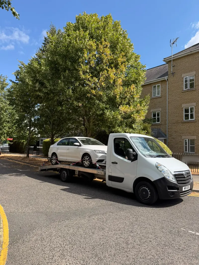 White SEAT Toledo loaded on the recovery truck on a tree-lined street